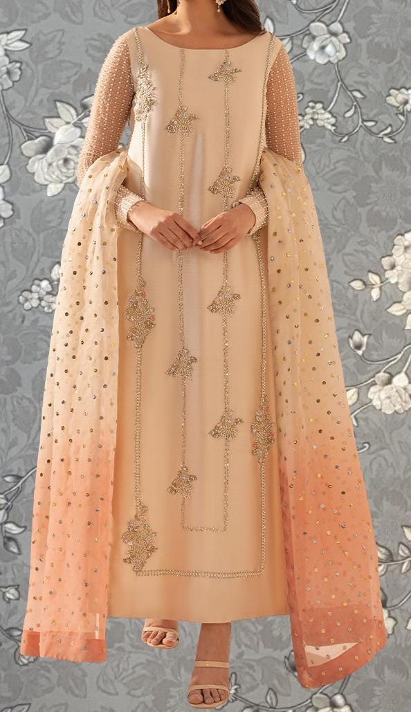 A woman wearing a long, beige dress with intricate embroidery and a matching shawl.