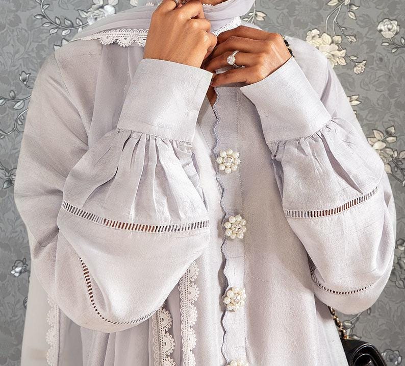 A person wearing a white dress with ruffled sleeves and a floral pattern on the background.