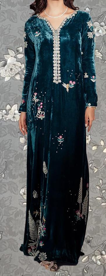 A woman wearing a long, green velvet dress with intricate floral embroidery on the bodice and sleeves.