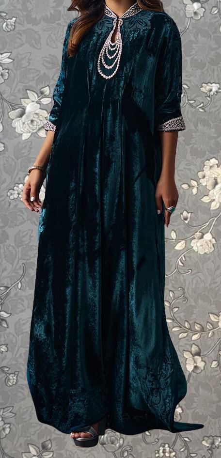 A woman wearing a long, dark green velvet dress with a floral pattern on the background.