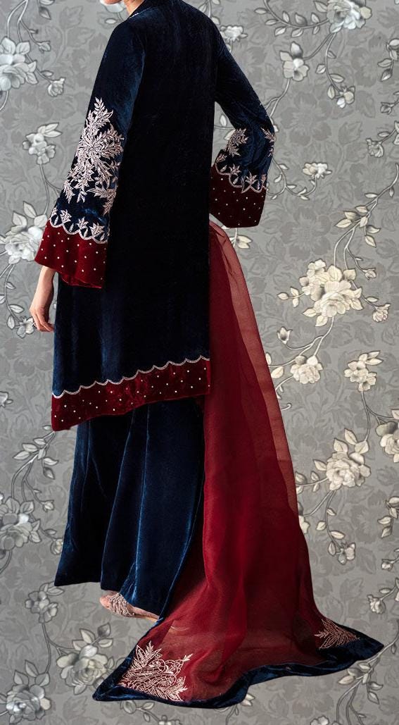 a person wearing a long, dark blue velvet dress with red accents, including a red train and a matching red skirt. The dress has a long, flowing skirt that extends behind the person, and the sleeves are decorated with red and white embroidery. The background features a gray floral pattern.