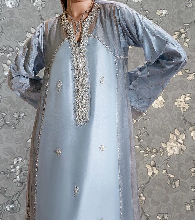 A woman wearing a light blue dress with intricate embroidery and a floral pattern on the background.