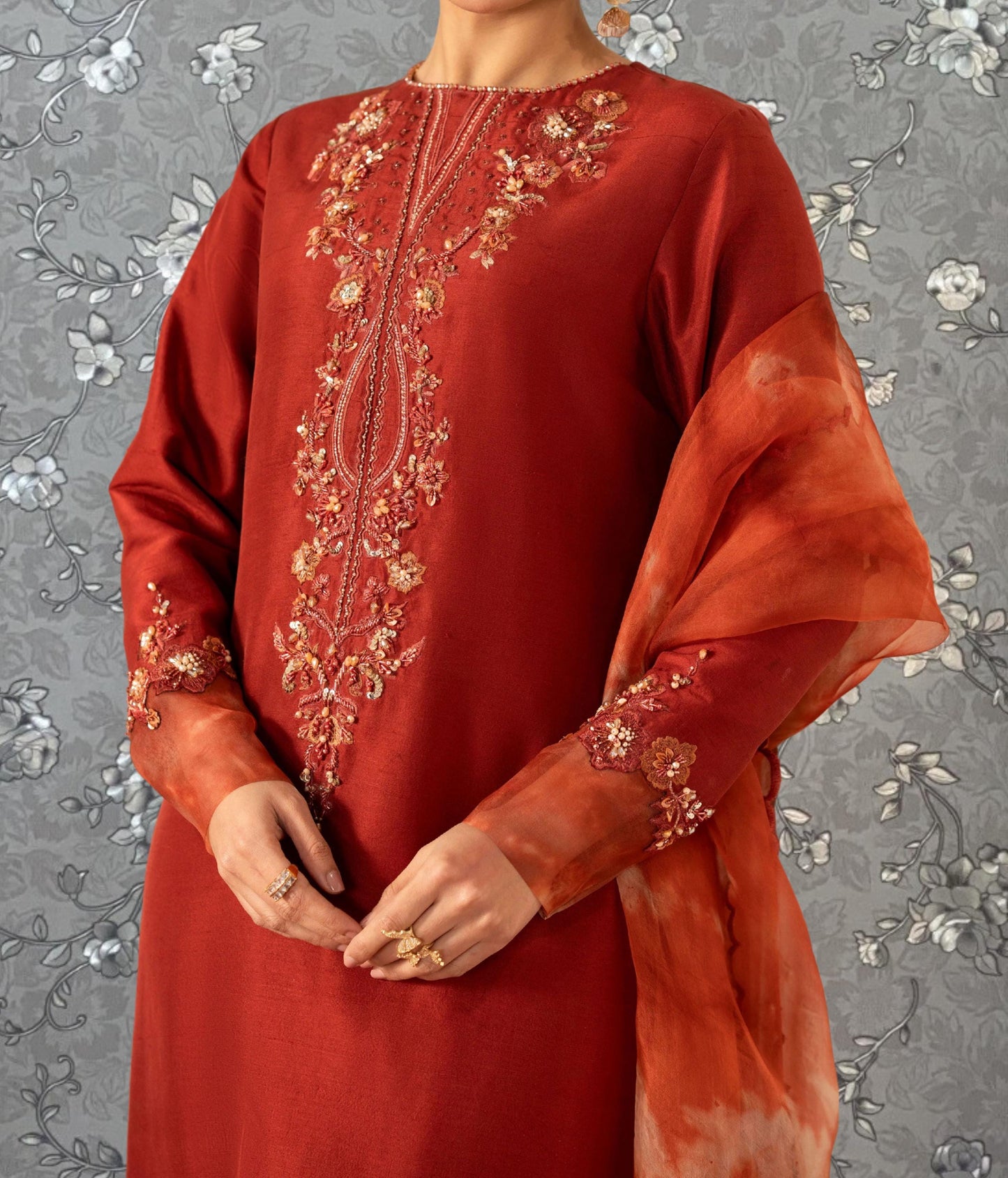 A person wearing a red dress with intricate embroidery and a matching red shawl draped over their shoulders.