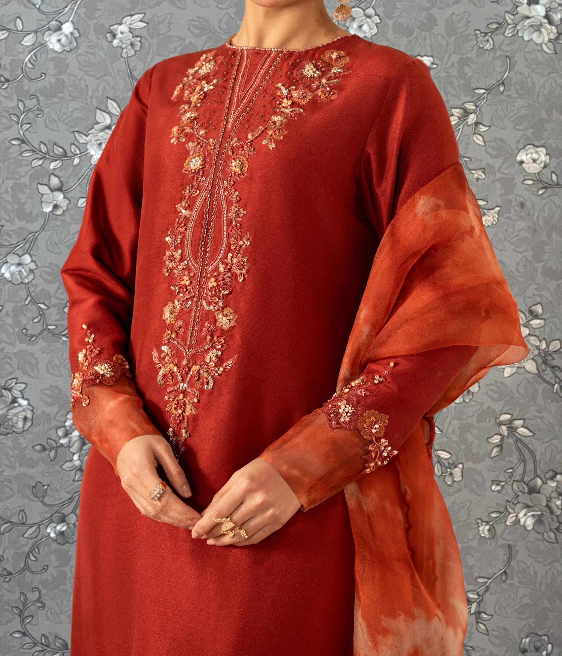 A person wearing a red dress with intricate embroidery and a matching red shawl draped over their shoulders.