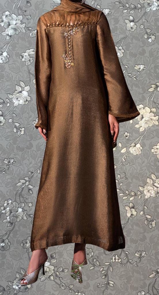 A person wearing a long brown dress with a floral pattern and high heels is standing against a gray floral background.