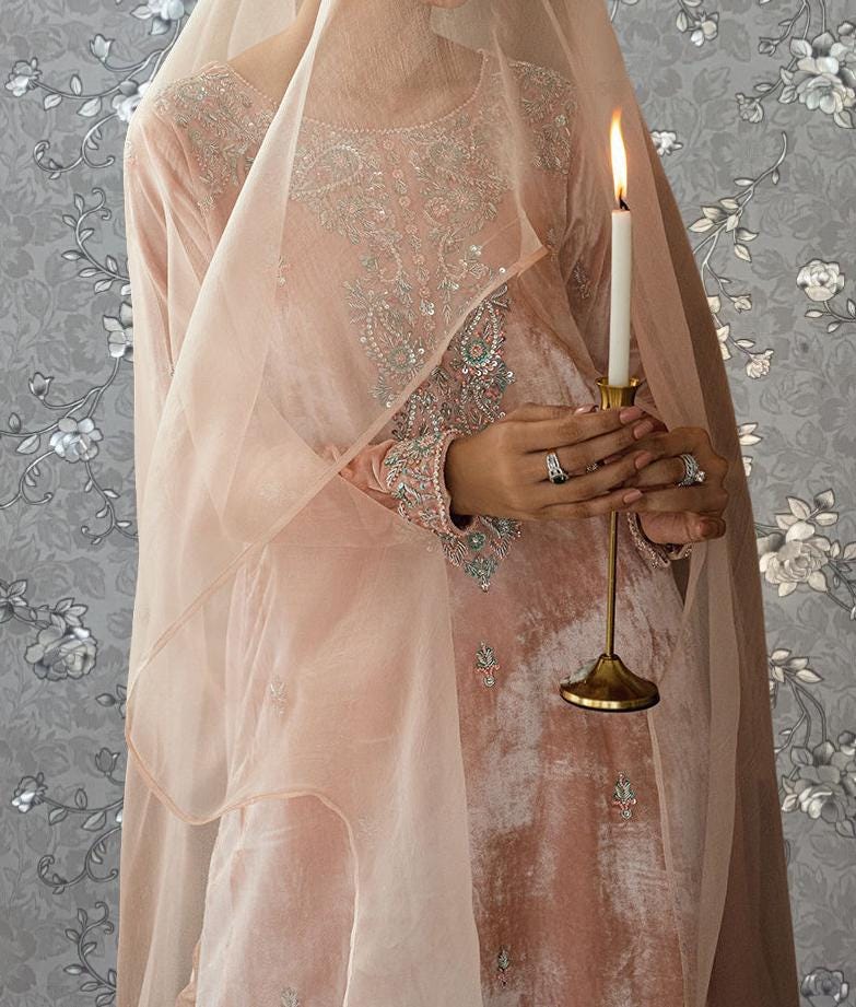 A woman in a pink dress holds a lit candle, with a floral patterned background.