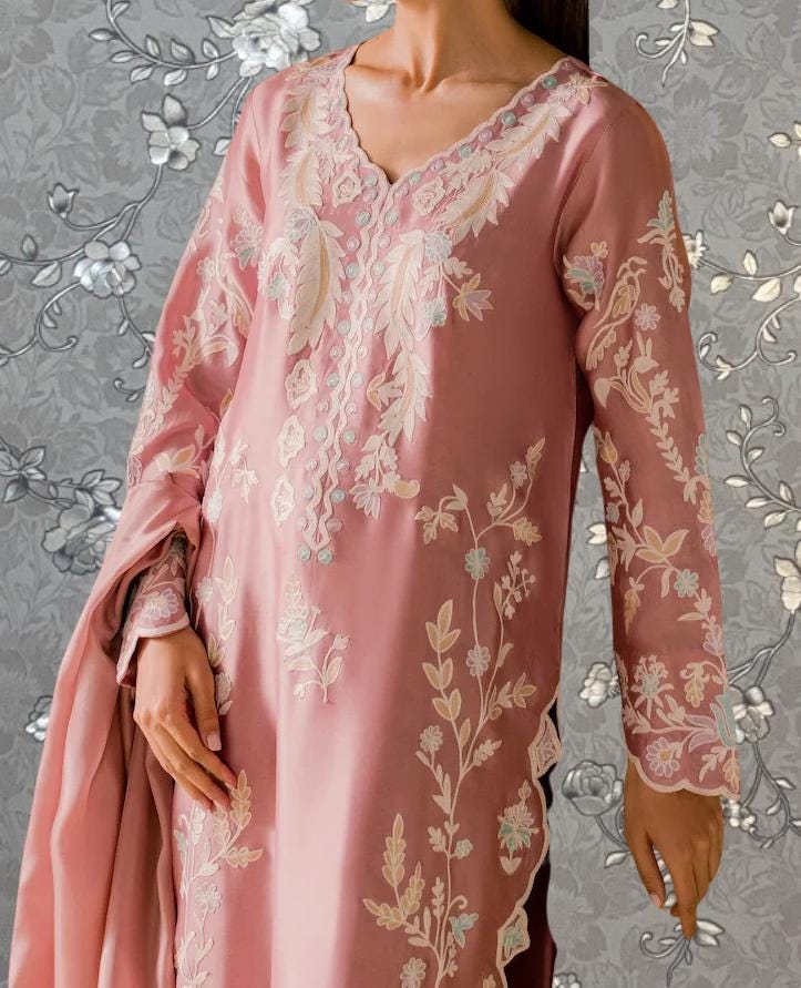 A close-up of a woman wearing a pink dress with intricate floral embroidery.