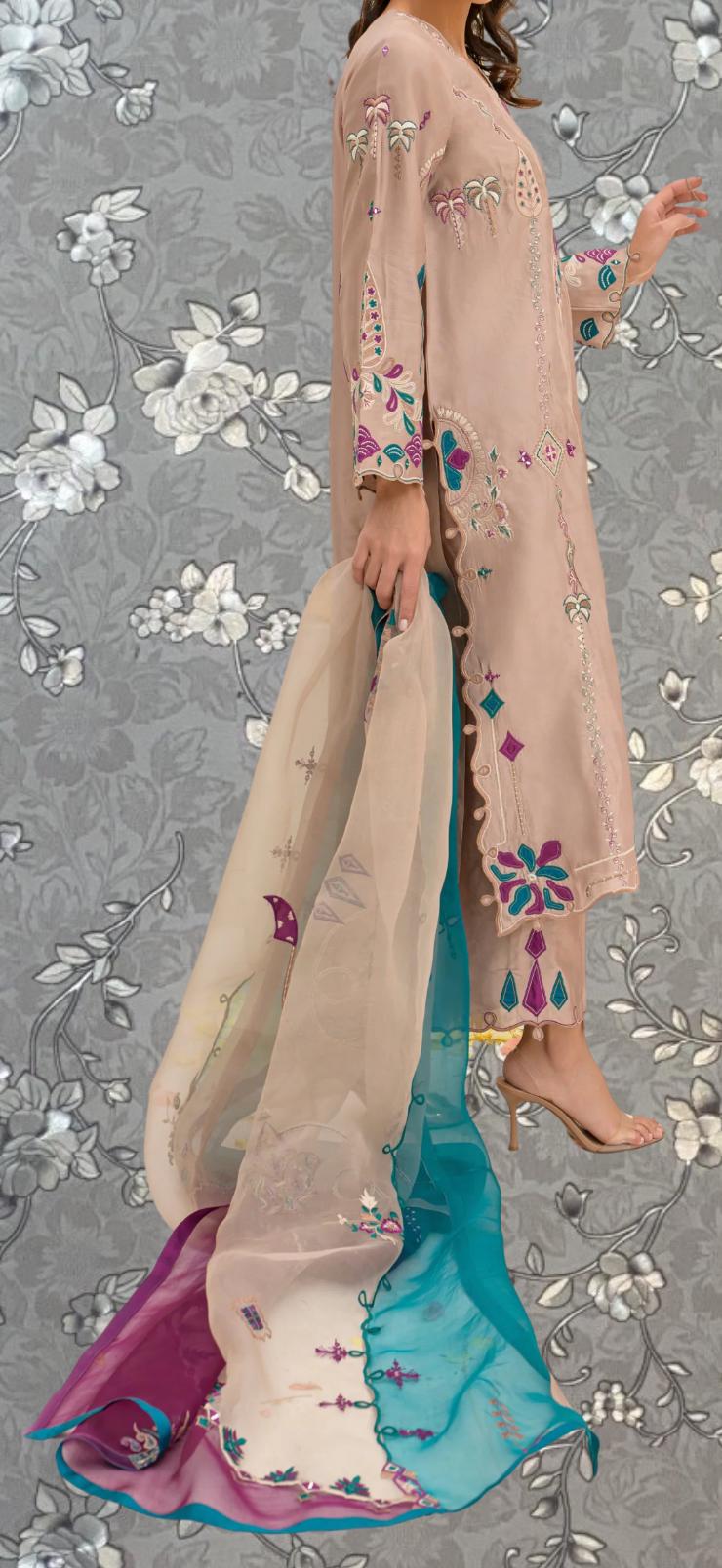 A woman wearing a long, light pink dress with intricate embroidered designs, standing against a gray floral background.