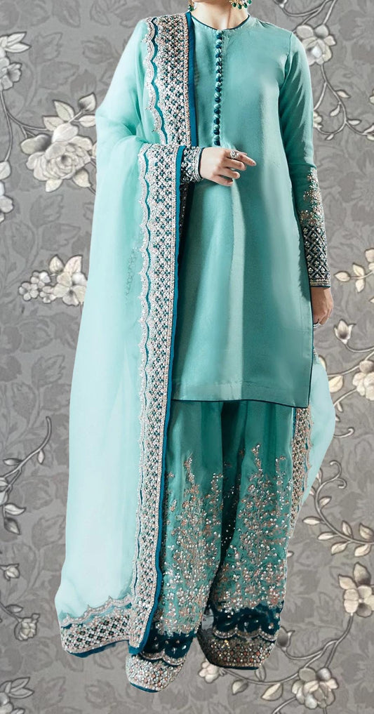 A person wearing a turquoise and white outfit with intricate embroidery and a matching turquoise shawl.