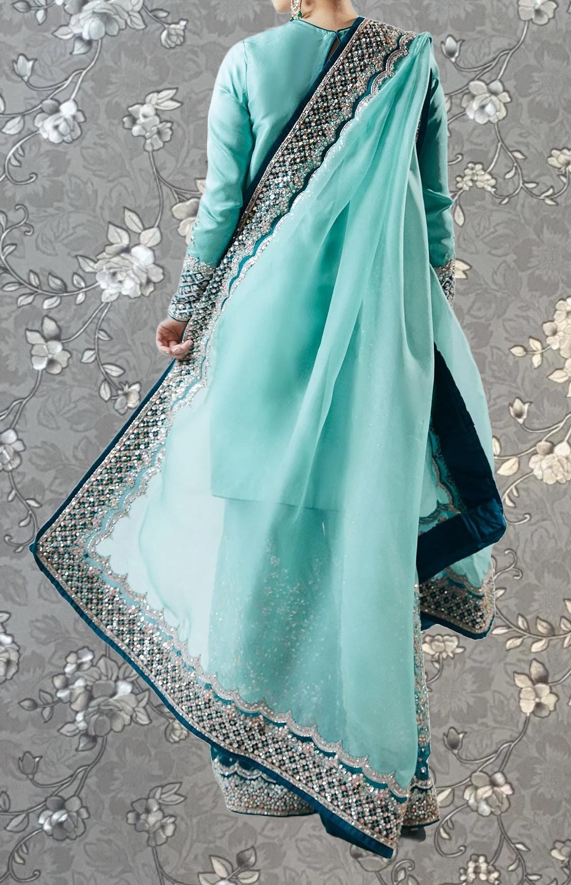 A person wearing a turquoise and blue patterned dress with a long, flowing skirt and a matching shawl.