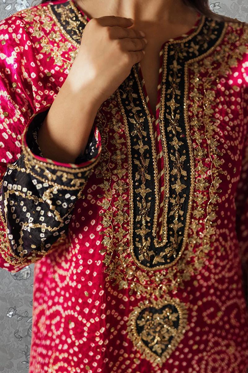 A close-up of a person wearing a vibrant red and black patterned dress with intricate embroidery and gold accents.