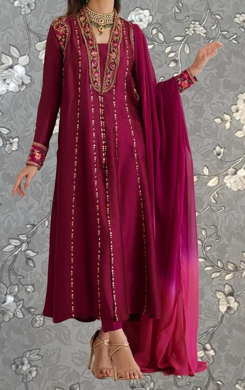 A woman wearing a long, burgundy dress with gold embroidery and a matching pink shawl. She is standing against a gray floral background.