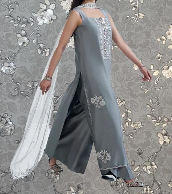 A woman wearing a gray dress with floral embroidery and a white shawl is walking against a gray floral background.