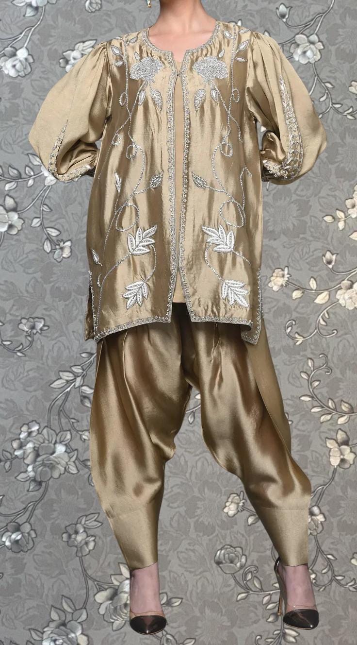 A gold-colored dress with intricate embroidery and a matching gold-colored jacket, both displayed on a mannequin against a gray floral background.