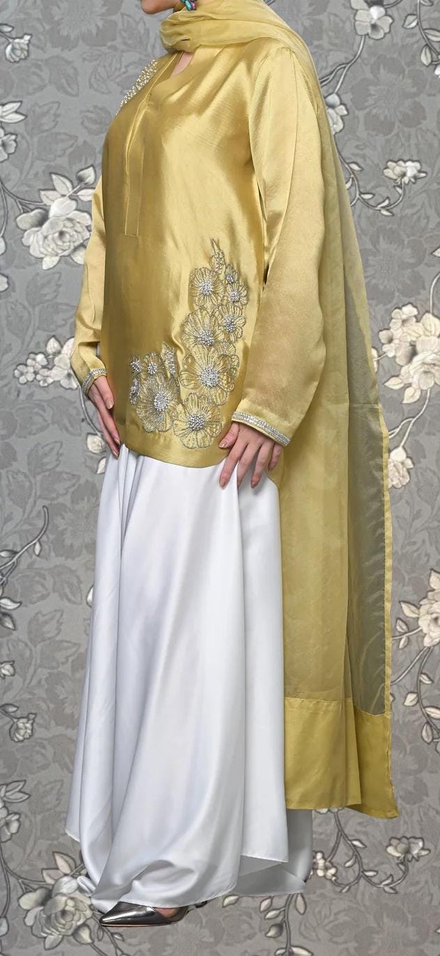 A person wearing a gold and white dress with a floral pattern on the top and a white skirt.
