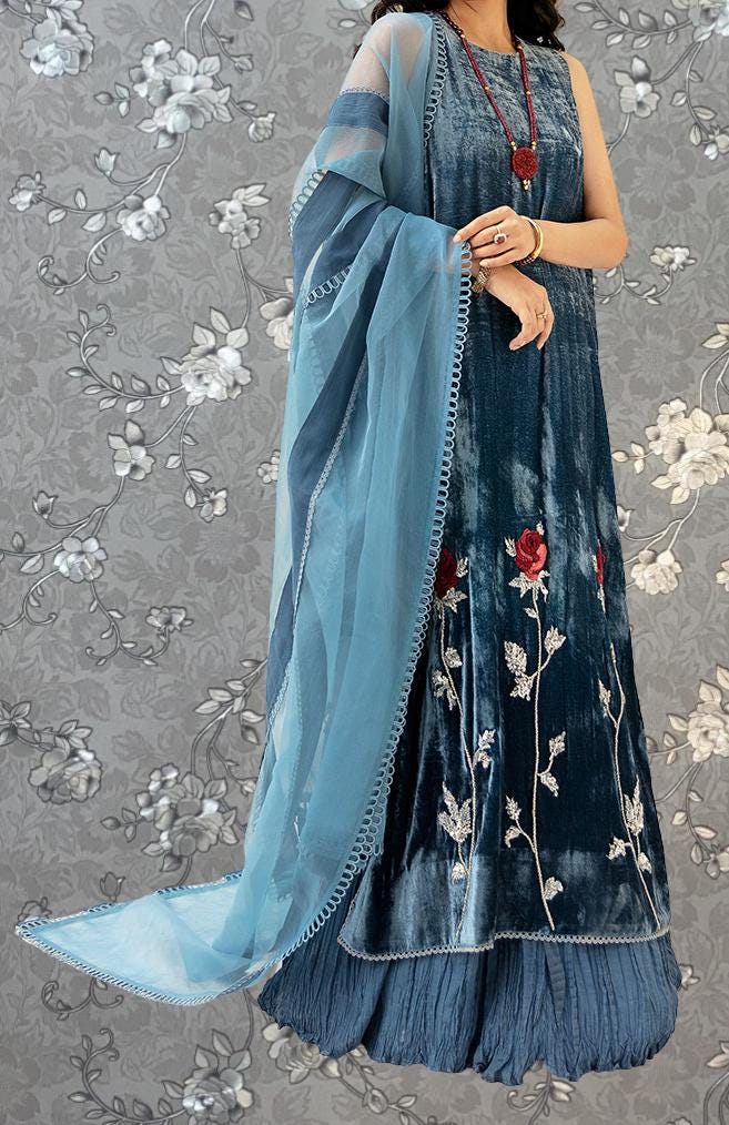 A woman wearing a blue and white dress with floral embroidery and a matching blue shawl.