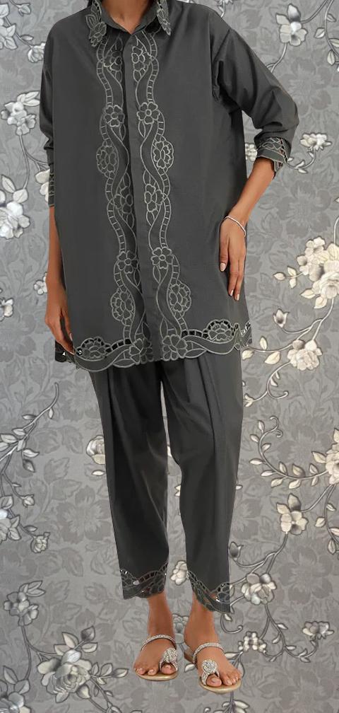 A person wearing a gray shirt with a floral pattern and gray pants stands against a gray floral background.