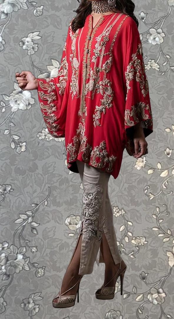 A woman wearing a red and gold patterned dress with a high slit on the left leg, standing against a gray floral background.