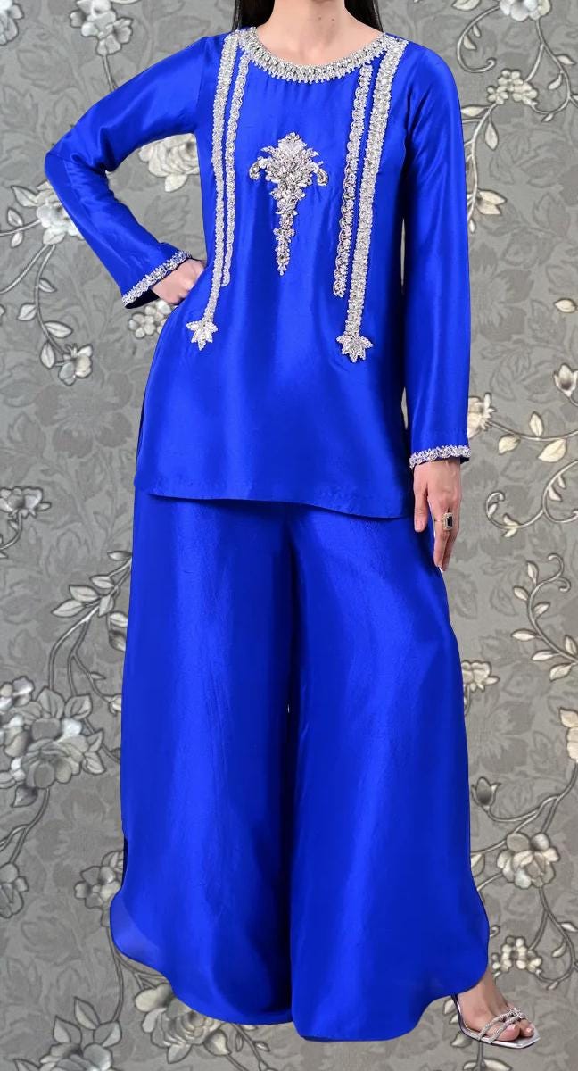 A woman wearing a long-sleeved blue dress with white embroidered designs on the front.