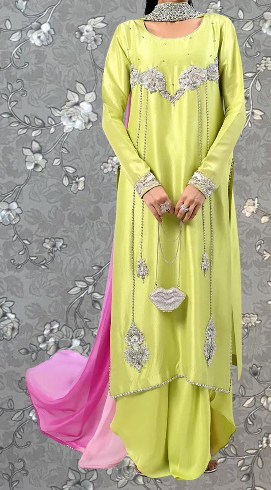 A person wearing a bright yellow dress with intricate embroidery and jewelry, standing against a gray floral background.