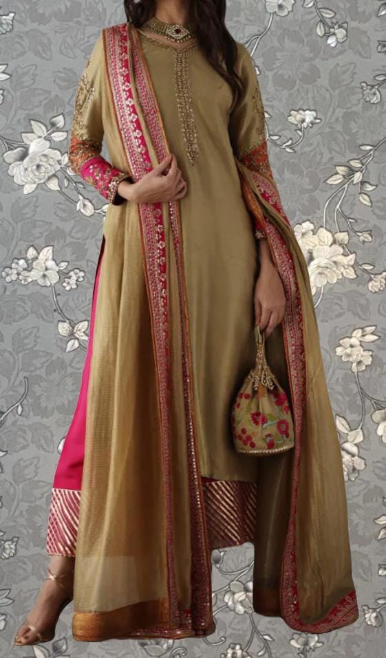 A woman wearing a gold and pink traditional Indian outfit, including a long shawl and a small purse, stands against a gray floral background.