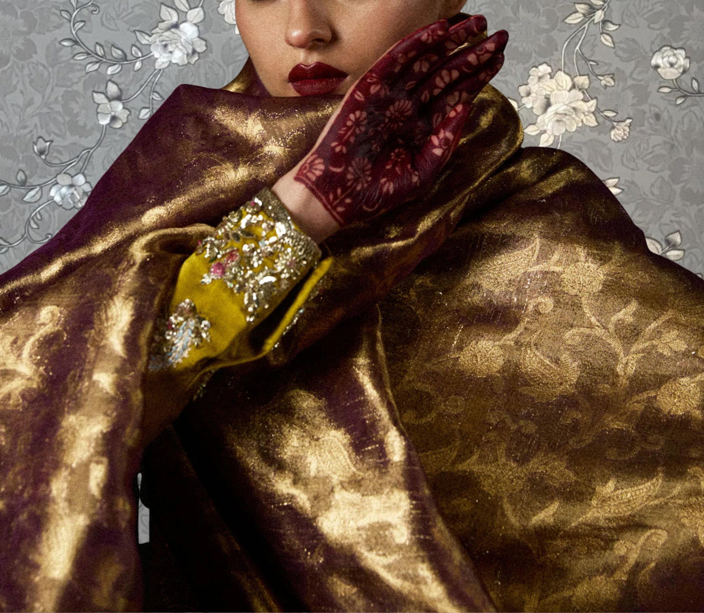 A close-up of a person wearing a gold and purple patterned garment, with a red and gold ornate bracelet on their wrist.