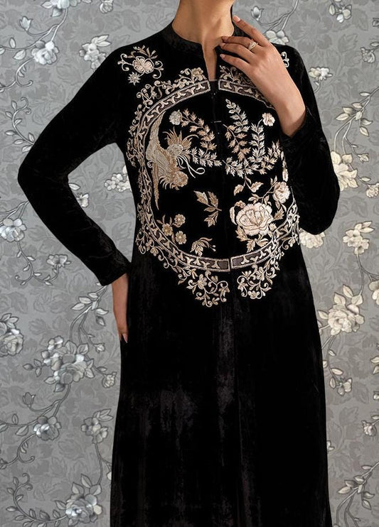 A person wearing a long black dress with intricate embroidered designs on the front.
