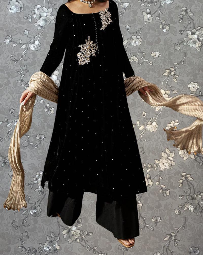 A woman wearing a black dress with a floral pattern and holding a beige scarf is standing against a gray floral background.