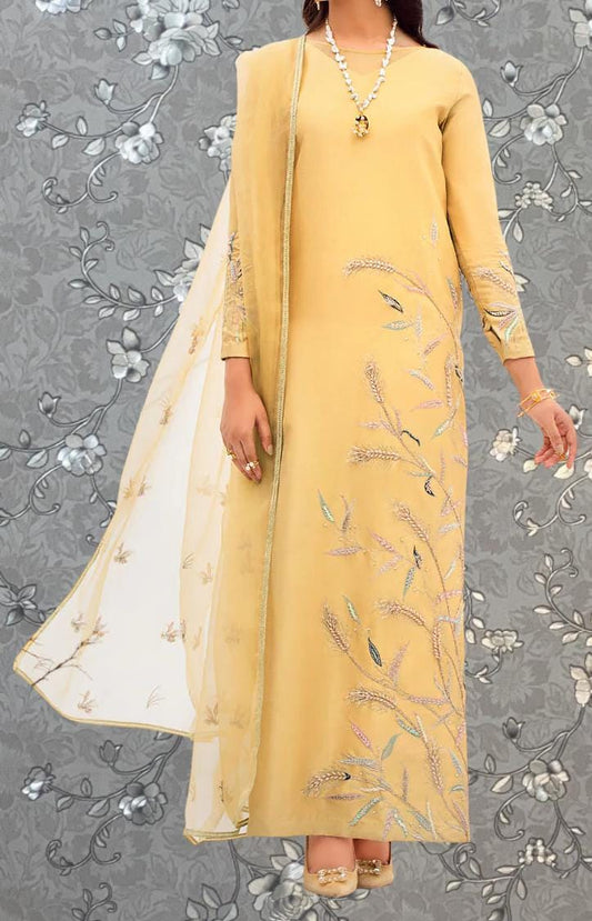 A woman wearing a long, yellow dress with intricate floral embroidery stands against a gray floral background.