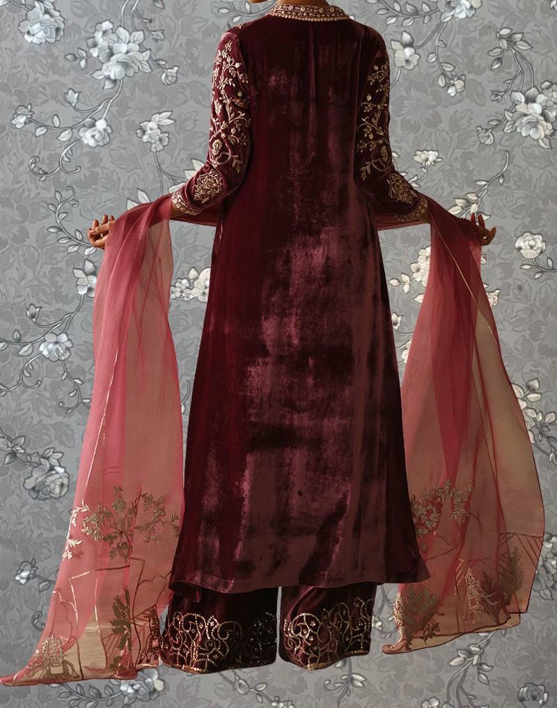A person wearing a long, burgundy velvet dress with gold embroidery and a matching red shawl.