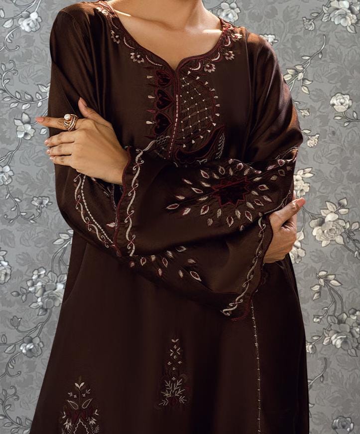 A woman wearing a brown dress with intricate embroidery stands against a floral background.