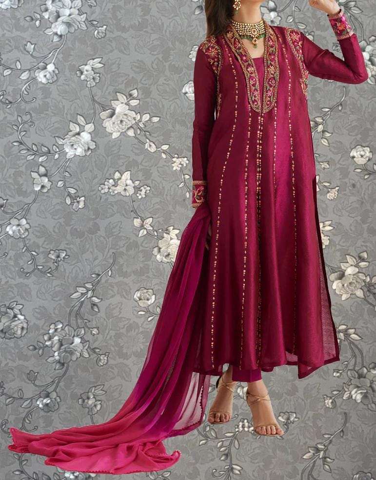 A woman wearing a long, burgundy dress with intricate embroidery and a matching pink shawl, posing against a gray floral background.
