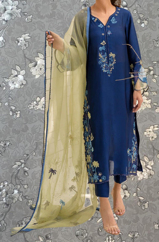 A woman wearing a blue dress with intricate embroidery and a yellow shawl is standing against a gray floral background.