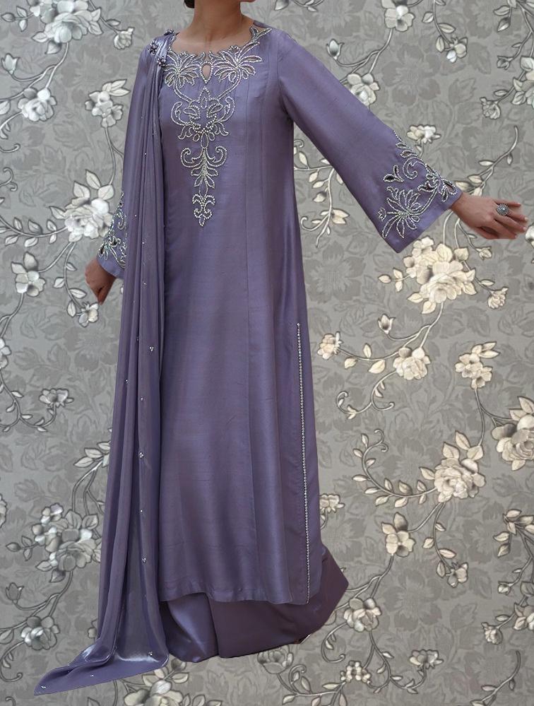 A woman wearing a long purple dress with intricate embroidery and a flowing cape.