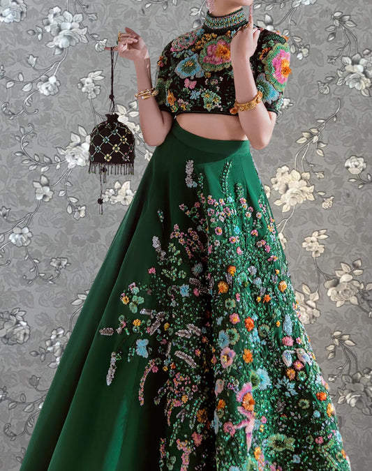 A woman wearing a green and pink floral dress with a high neckline and a black purse is posing against a gray floral background.