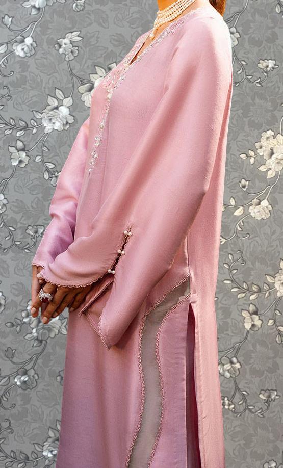 A woman wearing a long pink dress with a floral pattern stands against a gray and white floral background.