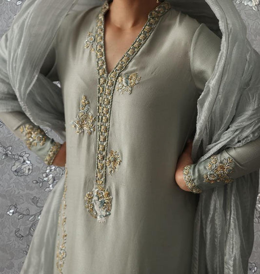 A close-up of a person wearing a gray dress with intricate embroidered patterns on the sleeves and collar.