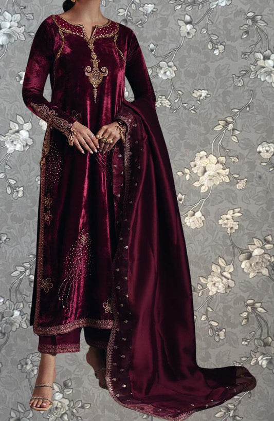 A woman wearing a long, burgundy velvet dress with gold embroidery and a matching shawl.