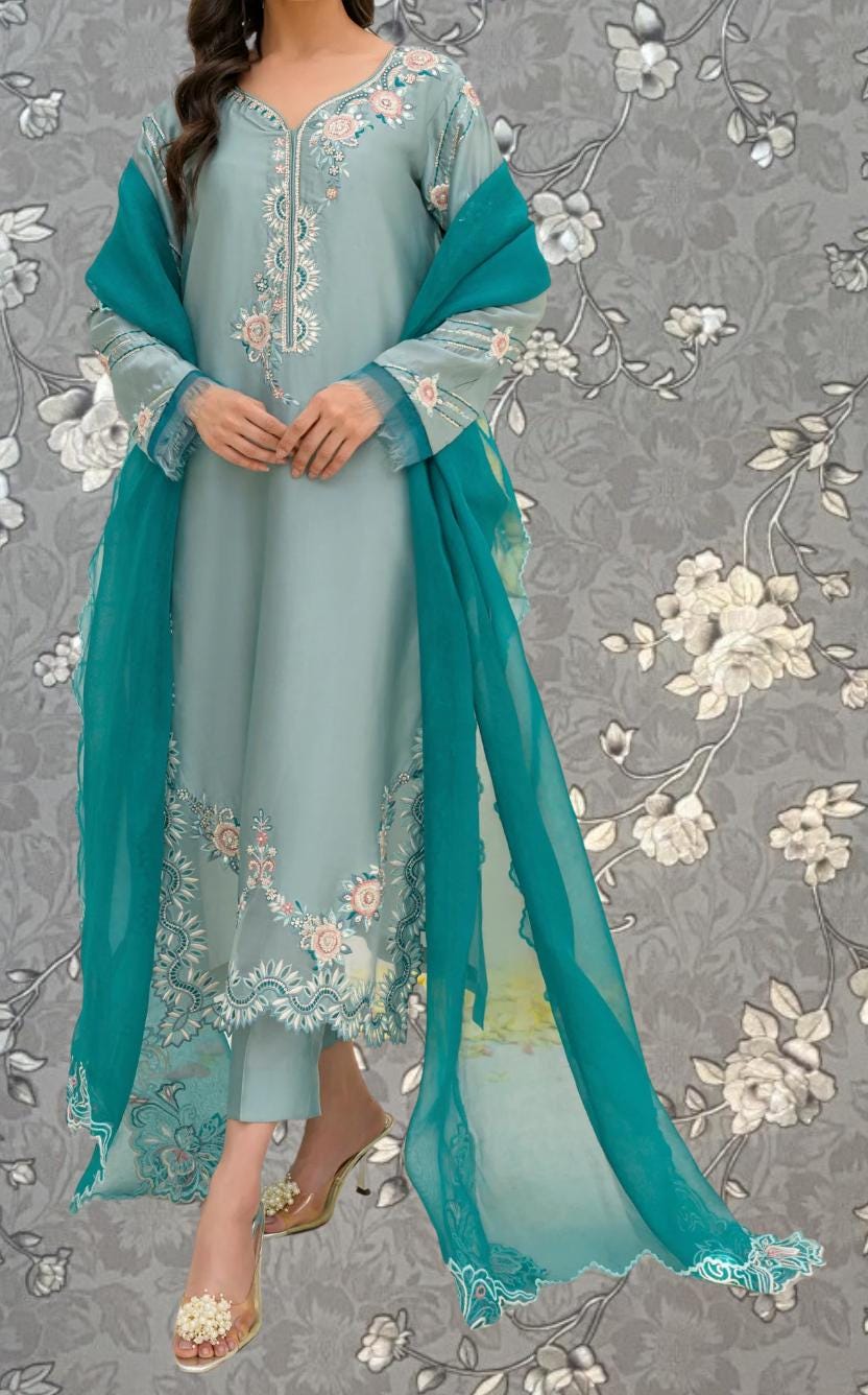 A woman wearing a light blue dress with intricate floral embroidery, standing against a gray floral background.