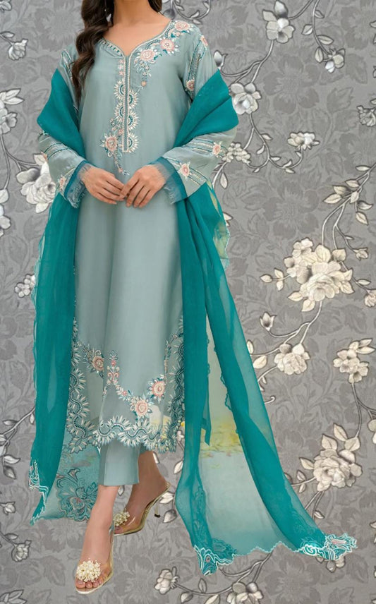 A woman wearing a light blue dress with intricate floral embroidery, standing against a gray floral background.