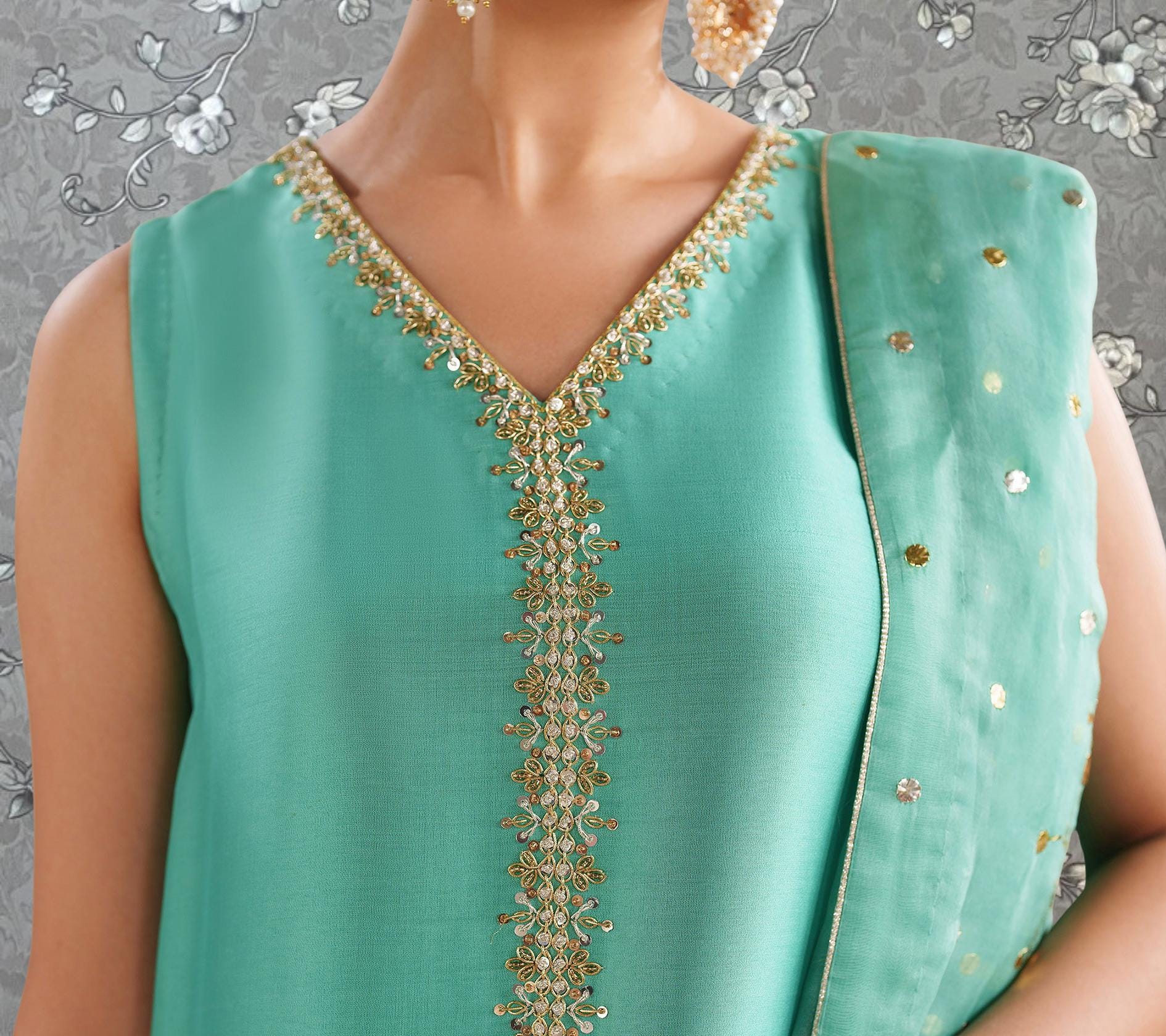 A close-up of a woman wearing a mint green dress with gold embroidery on the neckline and a matching green shawl draped over her shoulders.