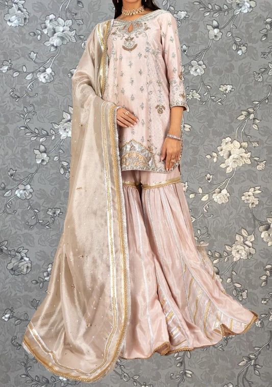 A woman wearing a pink and gold dress with a matching shawl, standing against a gray floral background.