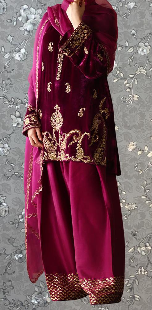 A person wearing a vibrant red and gold embroidered dress stands against a gray floral background.