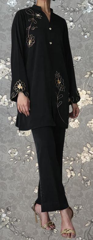 A person wearing a black dress with gold floral embroidery stands against a floral background.