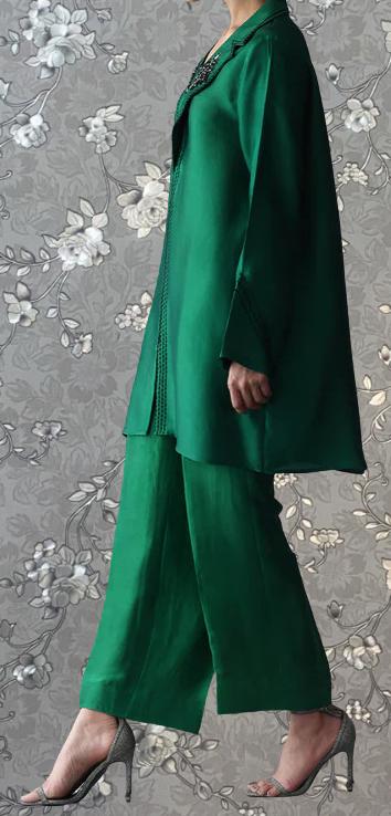 A person wearing a green jacket and matching pants, standing against a gray floral background.