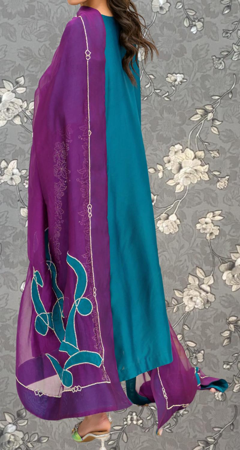 A woman wearing a purple and teal dress with intricate embroidery stands against a gray floral background.