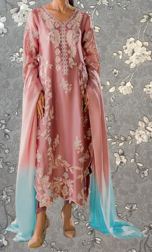 A woman wearing a pink and blue floral dress stands against a gray floral background.