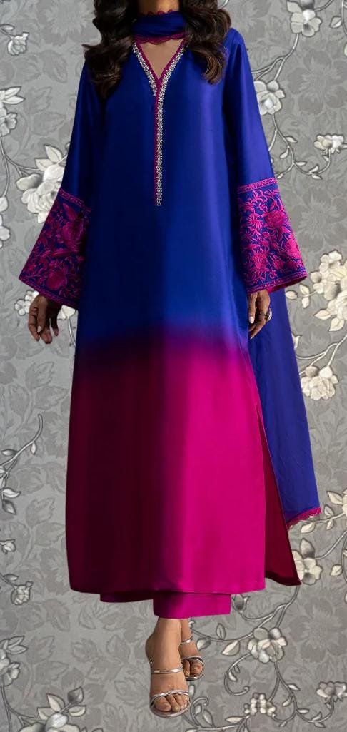 A woman wearing a long, blue dress with pink accents, standing against a gray floral background.