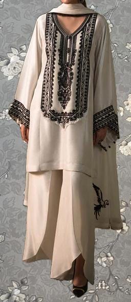 A woman wearing a long, cream-colored dress with intricate black embroidery and a matching skirt.