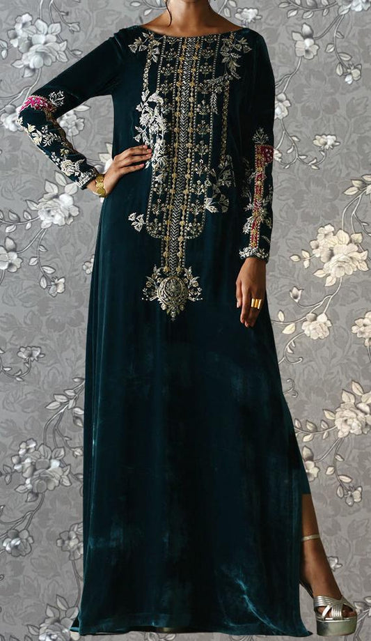 A woman wearing a long, dark green velvet dress with intricate gold embroidery and floral patterns.
